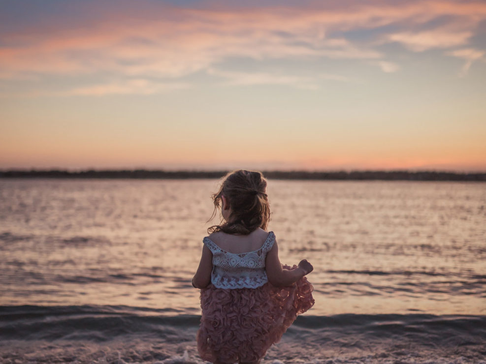 Portrait of a young girl in a dress standing in the water at sunset at Wrightsville Beach captured by Wilmington, NC family photographer Salty Star Photography