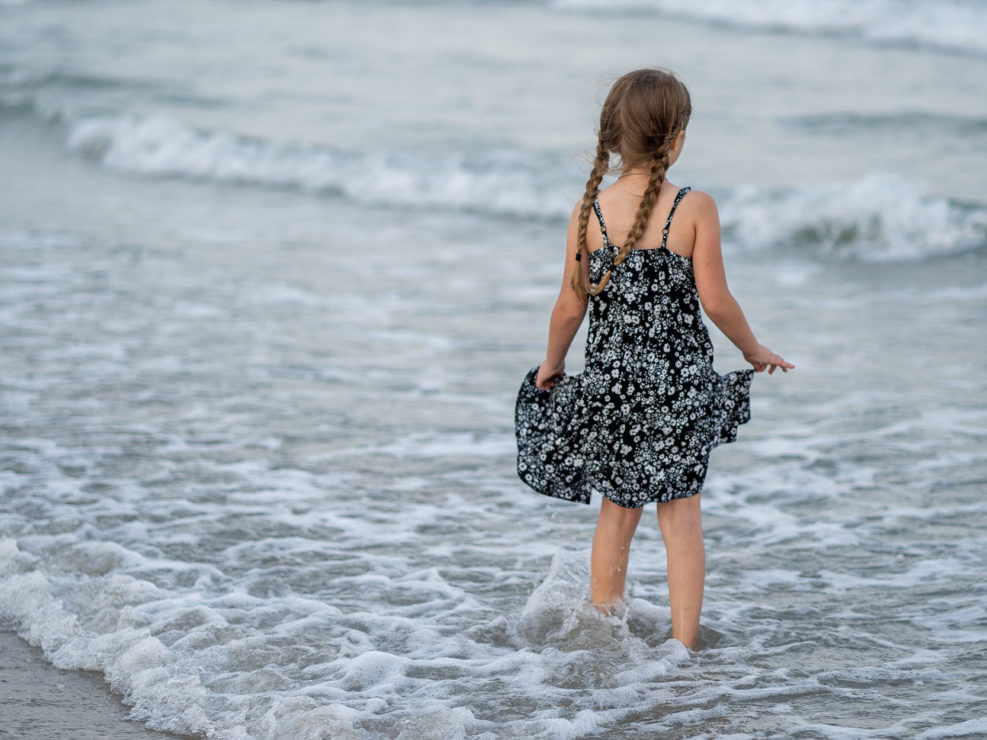 Portrait of a young girl in a floral dress and braided hair standing in the ocean at Wrightsville Beach captured by Wilmington, NC family photographer Salty Star Photography