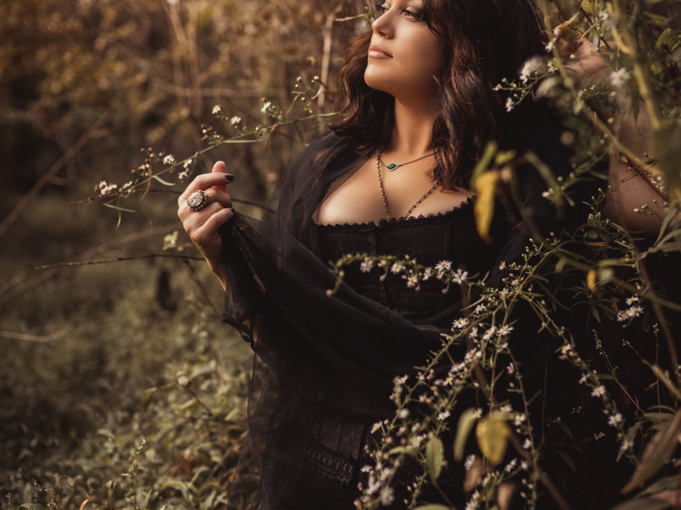 A portrait of a beautiful tattooed woman standing by white flowers in the swamp in NC captured by Wilmington, NC photographer Salty Star Photography