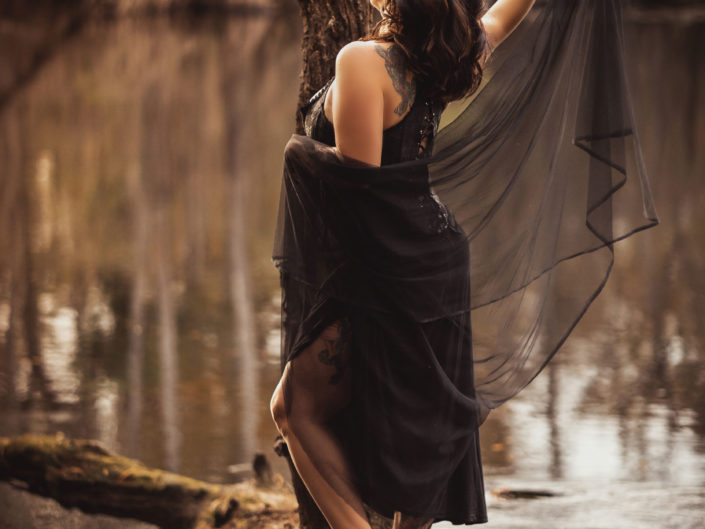 A portrait of a beautiful woman in a black corset standing on a tree branch by the Black River in NC captured by Salty Star Photography