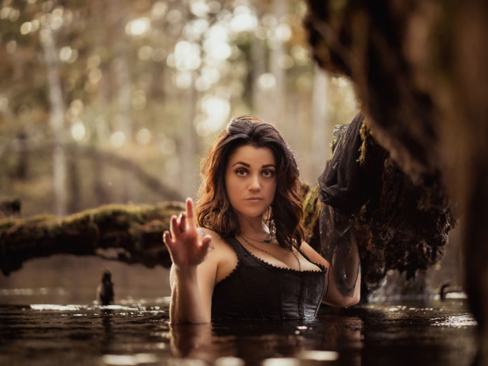 A beautiful woman in a black corset standing in the Black River by a moss covered tree branch at the Black River in Kelly, NC captured by Salty Star Photography