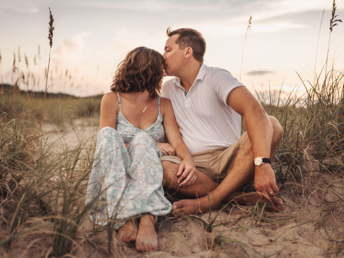 A portrait of a married couple sitting among the sea oats and embracing on the beach at Fort Fisher, NC captured by Salty Star Photography