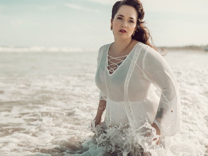 Beach boudoir portrait of a woman in a white dress with waves crashing on her at Wrightsville Beach, NC captured by Salty Star Photography