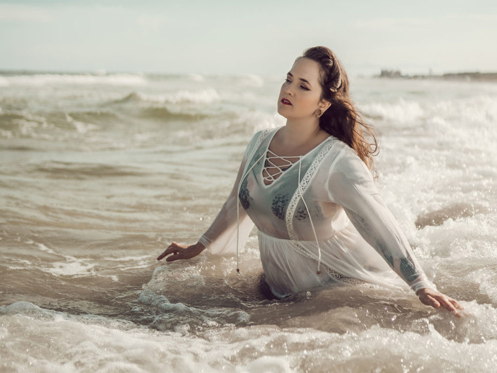 Beach boudoir portrait of a woman in a white dress with waves crashing on her at Wrightsville Beach, NC captured by Salty Star Photography