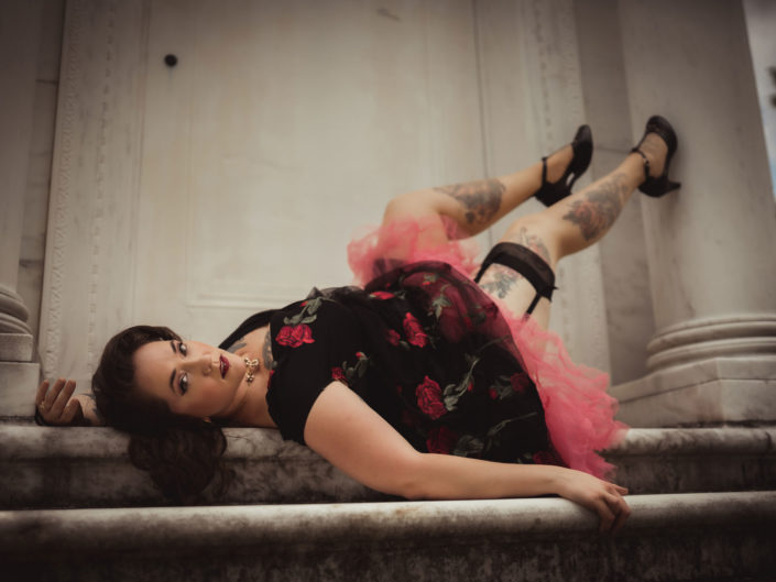 Pinup model laying on marble stairs wearing a rose dress in Wilmington, NC captured by Salty Star Photography
